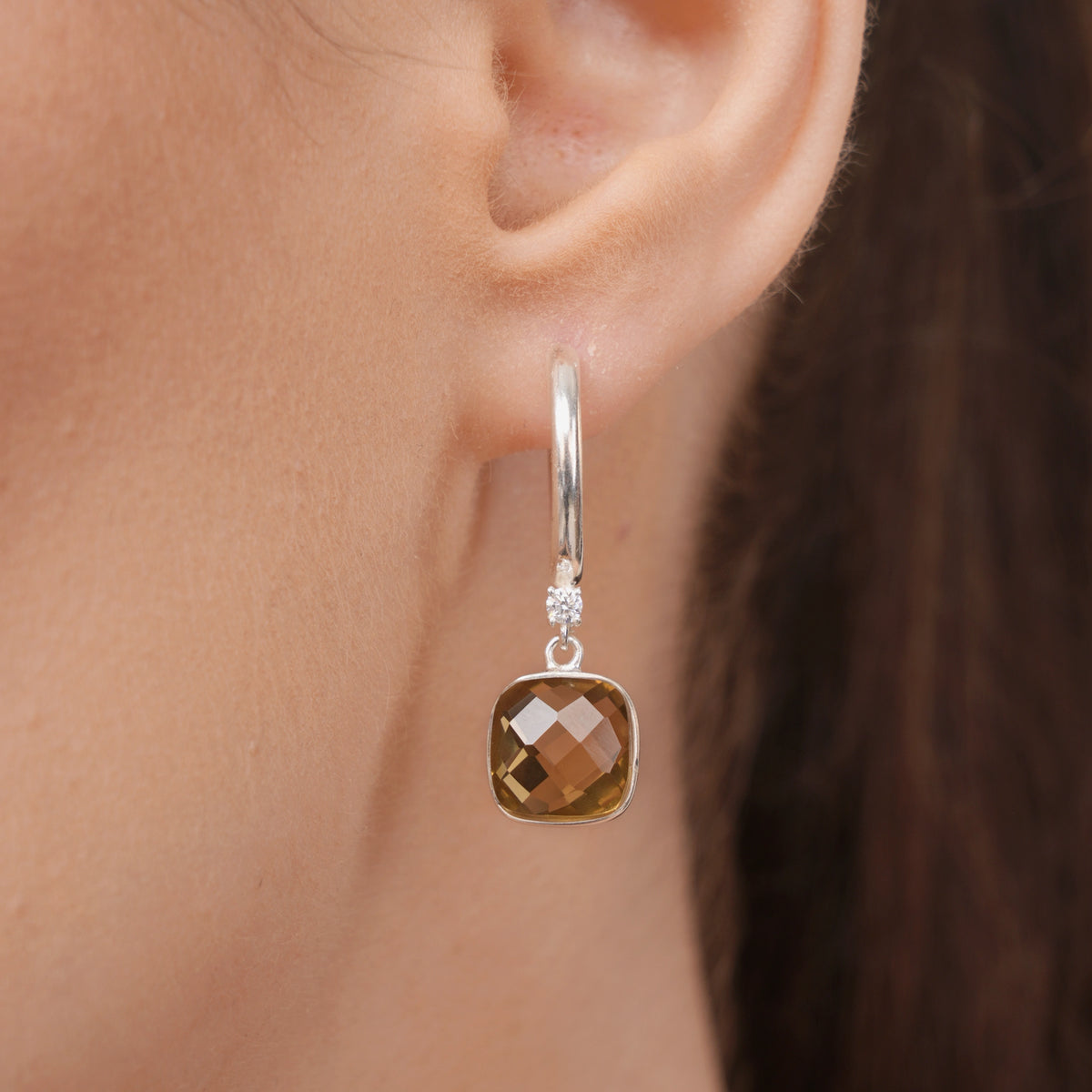 Detailed view of an Olive Quartz drop hoop earring worn on the ear, highlighting the faceted stone and small clear accent.