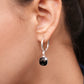Close-up of a sterling silver drop hoop earring worn on the ear, with a faceted black garnet below a small clear stone.