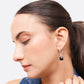 Three-quarter profile of a model wearing a black garnet drop hoop earring, showing its length below the earlobe.