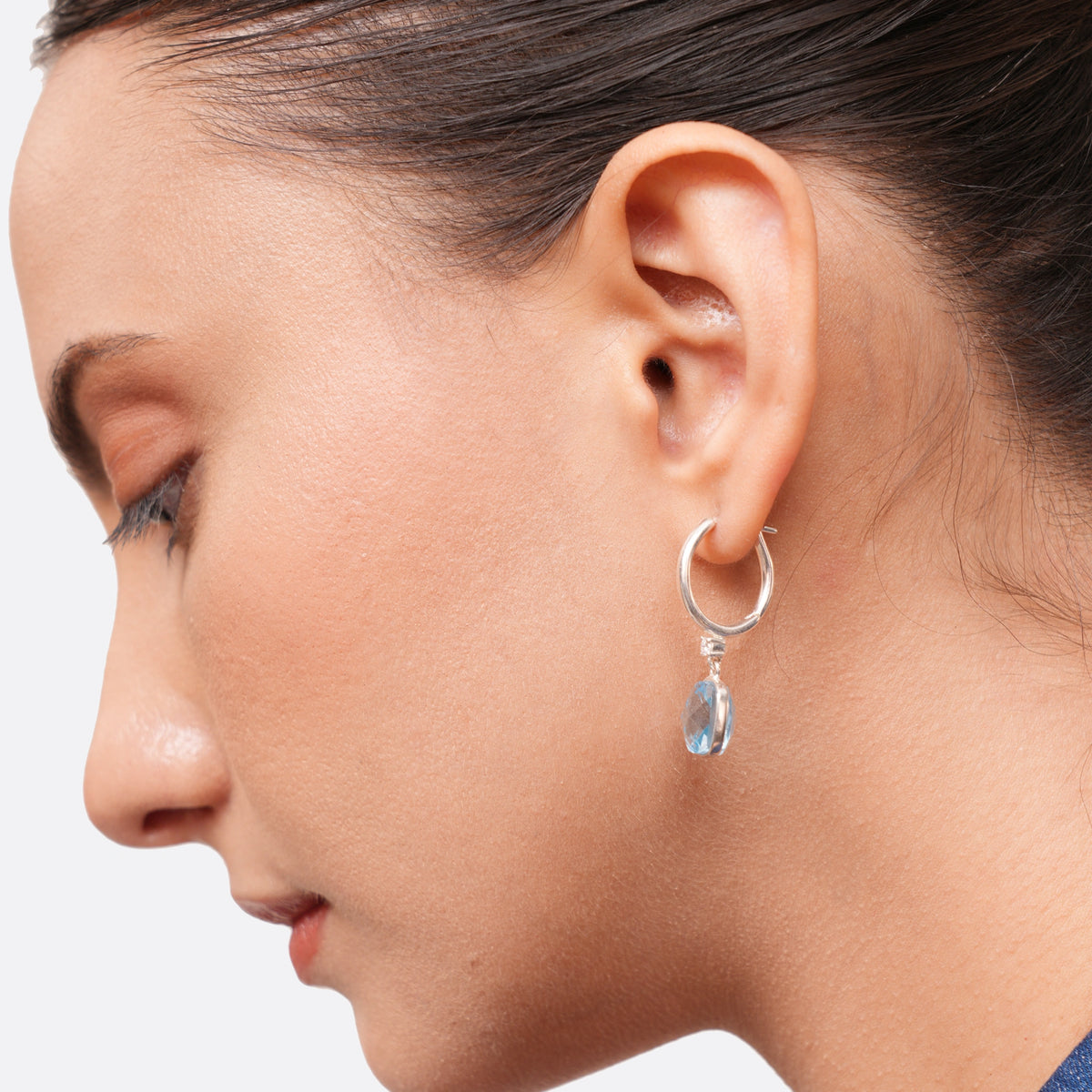 Close side view of a silver drop hoop earring worn on the ear, revealing the curved hoop and the depth of the aqua chalcedony.