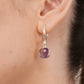 Close-up of a sterling silver hoop earring worn on the ear, displaying a brilliant-cut accent stone above a violet amethyst.