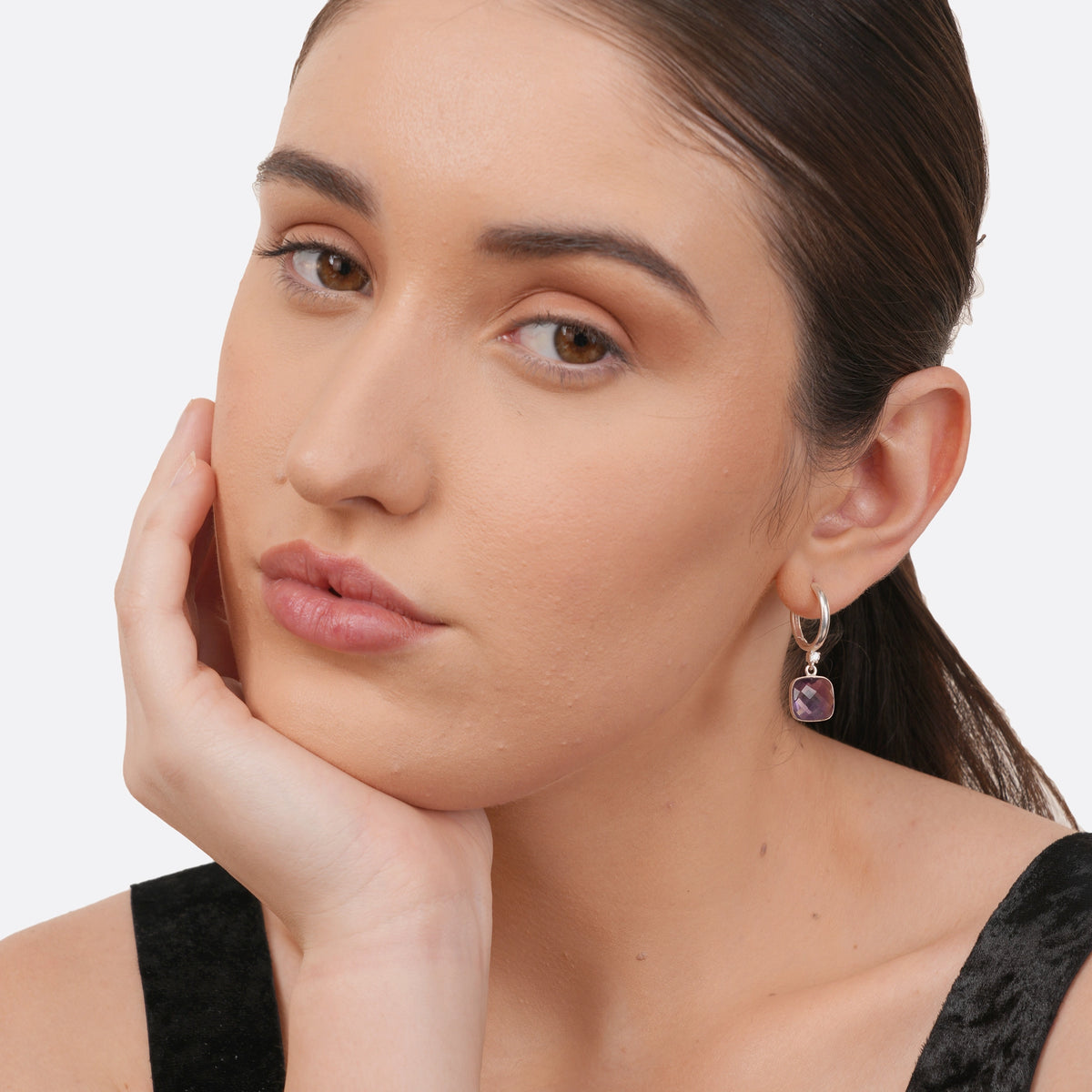 A model photographed at a slight angle wearing The Lumi Edit silver hoop earrings with vivid violet amethyst drops.