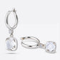 White Topaz drop hoop earrings presented against a white background, with one upright and the other resting flat to show depth.