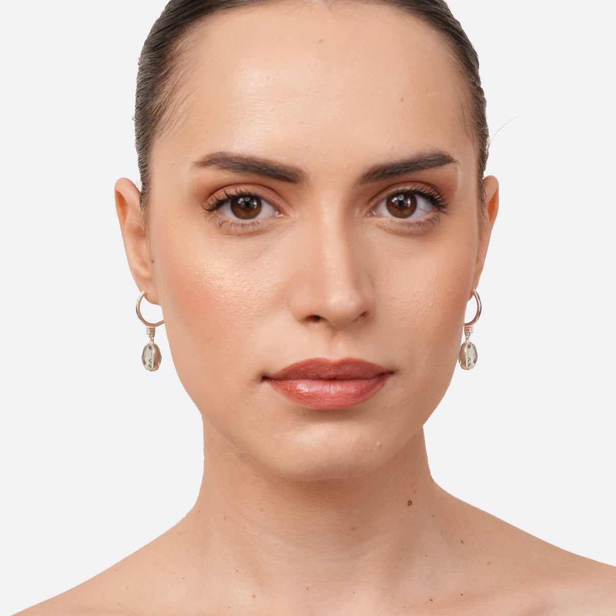 A model facing forward wearing RILAVE Green Amethyst drop hoop earrings, with faceted stones suspended beneath silver hoops.