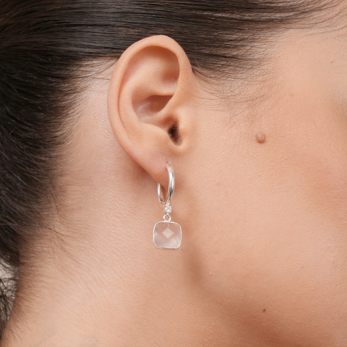 Rose Quartz drop hoop earring worn on the ear, featuring a cushion-shaped pink gemstone suspended from a polished silver hoop.