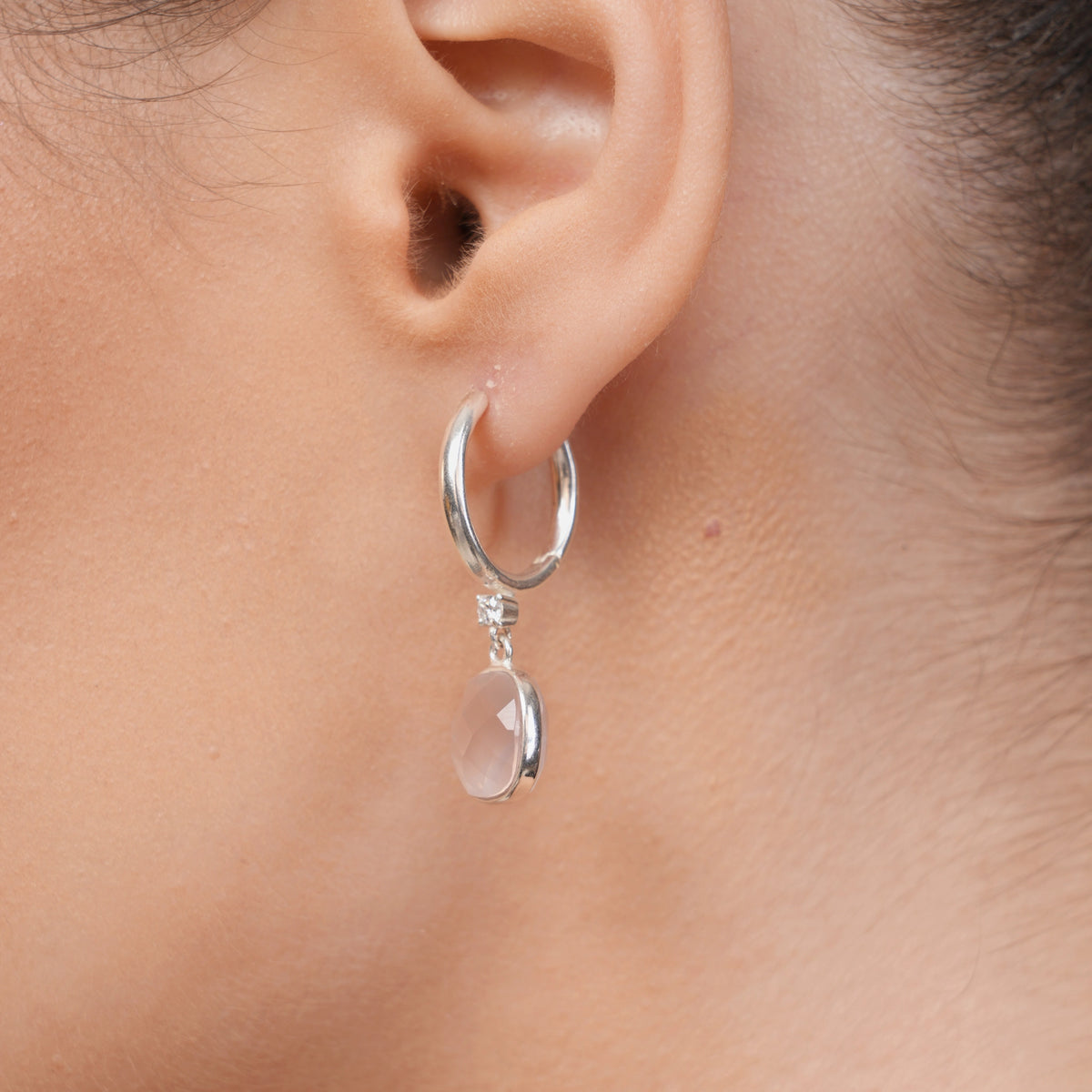 Side view of a RILAVE Rose Quartz drop hoop earring worn on the ear, highlighting the silver hoop and pale pink gemstone setting.